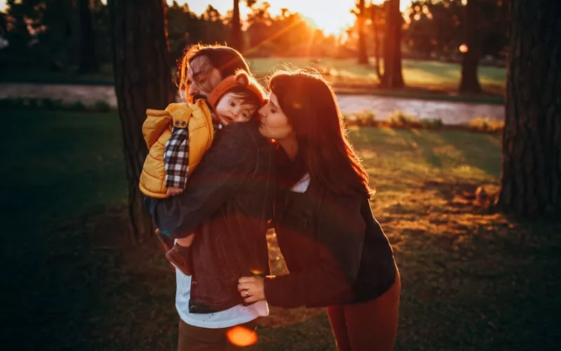 Parents hugging their young son together in a park at sunset
