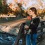 Mother carrying her baby in a front baby carrier while standing on a wooden bridge in a park.