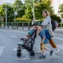 Woman walking across a city street with two children, pushing a stroller during a trip.