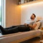 Modern wellness setup with a man relaxing on a bed wearing sleek black compression boots.