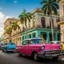 Colorful vintage cars driving through Havana streets with colonial buildings.