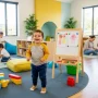 A happy child playing in a bright, modern daycare and preschool environment, with a mix of learning activities.