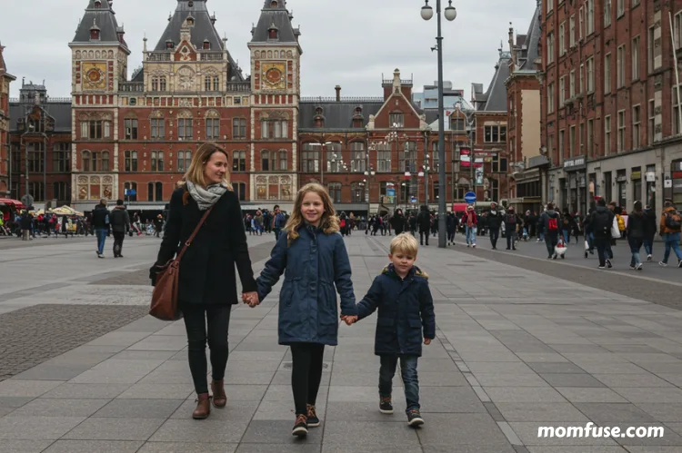 A mom and two kids walking hand-in-hand near Amsterdam Centraal Station.
