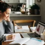 A modern mother studying nursing at home, sitting at a kitchen table with a laptop and notebooks.