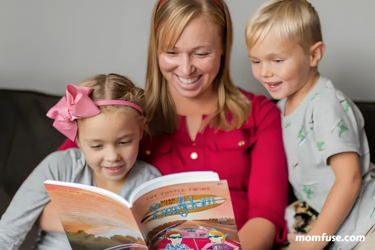 Smiling mother reading a book titled “The Tuttle Twins with her two young children.