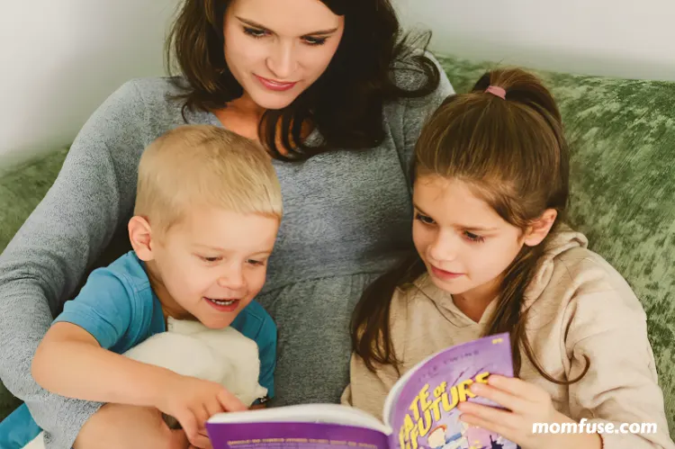 Mother reading with her two children as they look at a book.