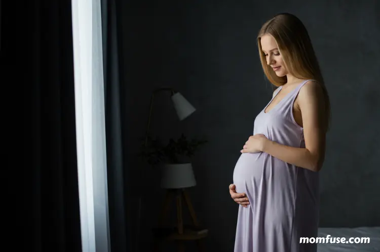 Pregnant woman in a darkened bedroom with blackout curtains gently filtering light.