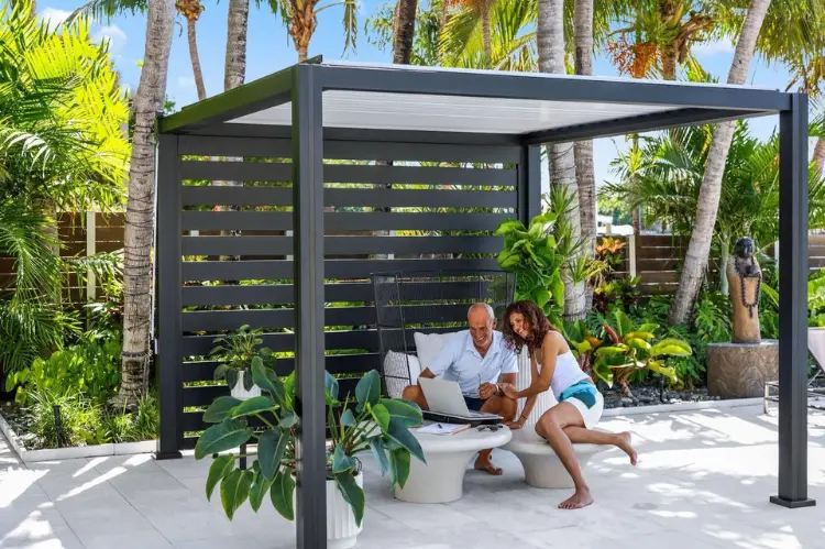 Cozy outdoor patio with a manual K-BANA™ pergola, person adjusting louvers by hand.