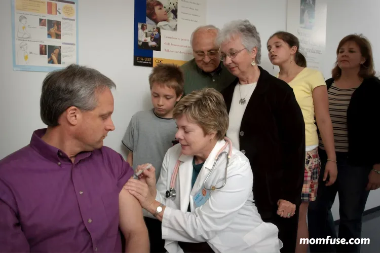 A doctor administers a vaccine to a man while several people, including children and seniors.