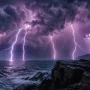 Lightning strikes over a stormy ocean beside a rocky coastline at night.