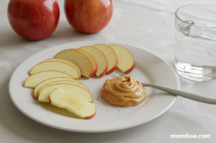 Healthy afternoon snacks on a plate—apple slices with peanut butter and a glass of water.