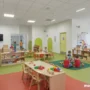 Modern daycare center with playful, colorful classrooms, children playing safely, and discreet security cameras.