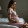 A pregnant woman in cozy sleepwear sitting on the bed serene and relaxed.