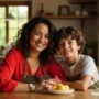 A smiling mother and her young son sitting at a wooden kitchen table.