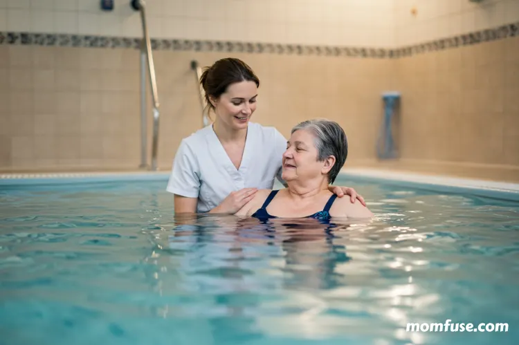 A friendly female hydrotherapy in a white uniform is assisting an elderly woman.