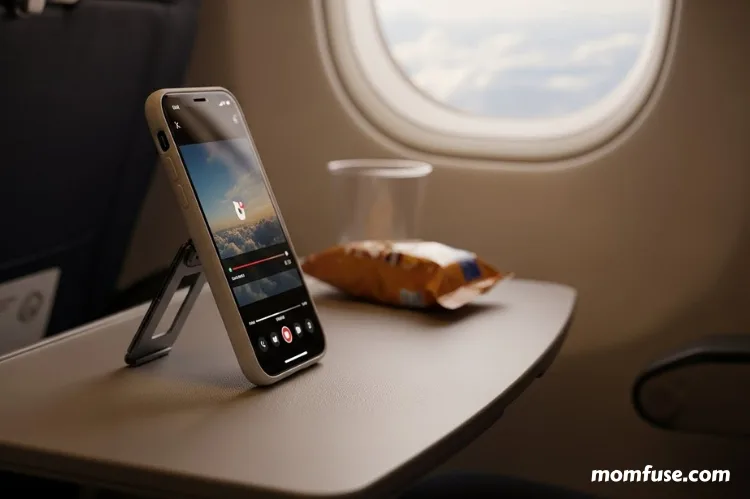 iPhone with magic stand case on an airplane tray table, phone standing securely while playing video.