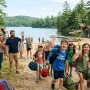 happy children at summer camp near lake and cabins, parents waving goodbye, outdoor adventure.