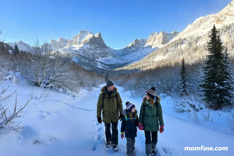 Realistic winter travel scene showing a family walking through a snowy U.S. landscape with mountains.