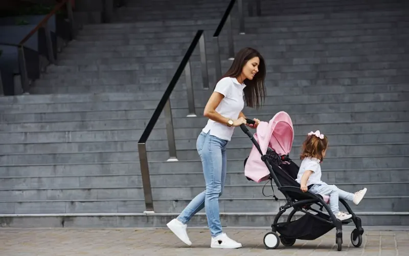 Woman pushing a stroller with a young child along a city sidewalk.